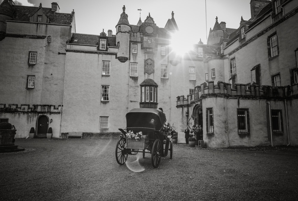 Black and white image of a bride arriving at Fyvie Castle for her wedding in a horse and cart