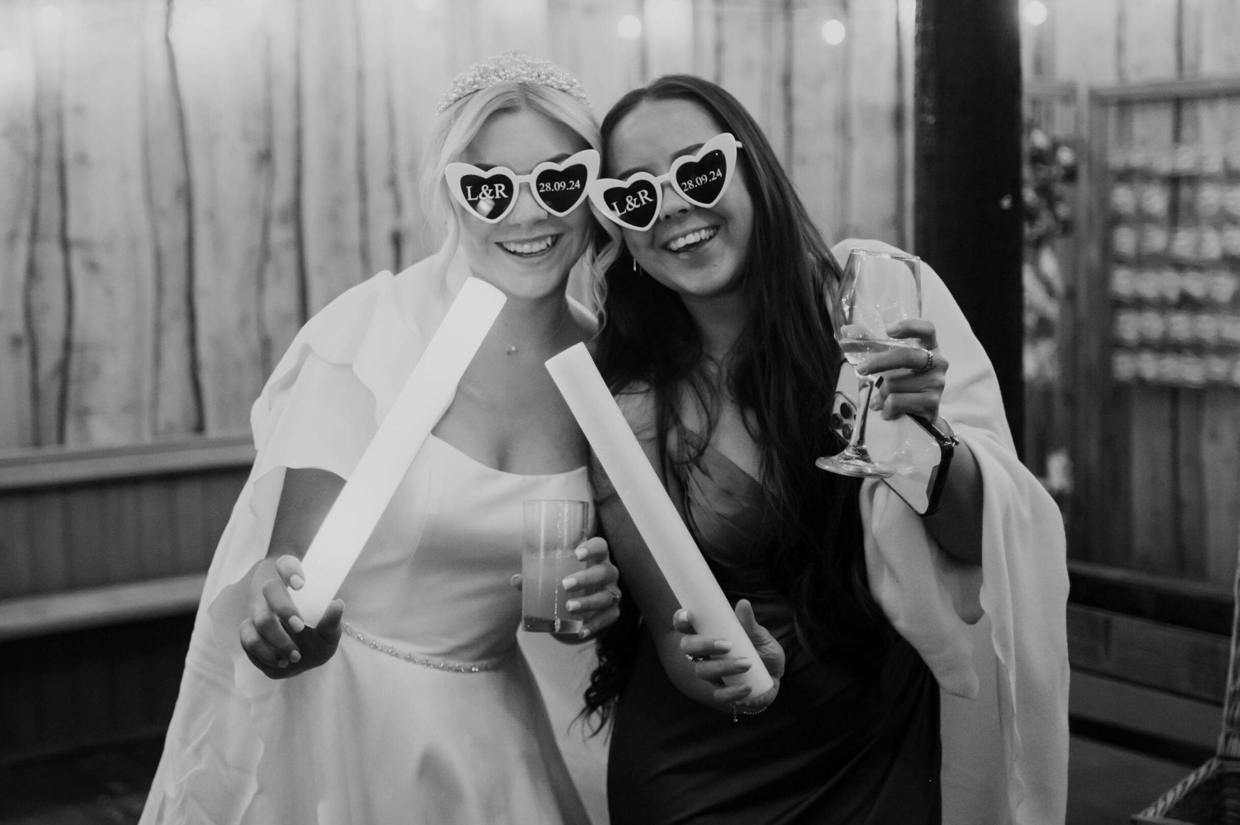 A bride and friend smile wearing heart shaped sunglasses captured by Zoe Rae, wedding photographer