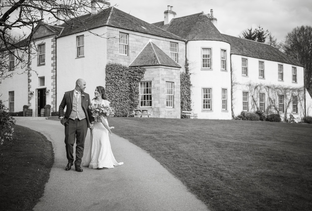 Bride and groom walk in front of the house taken by Zoe Rae Photo